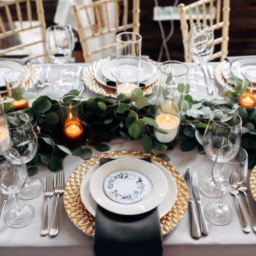 Decorated table with gold plates, candles and greens on the white tablecloth